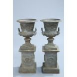 A HANDSOME PAIR OF CAST IRON URNS ON PLINTHS, of campana form, the plinths with a laurel wreath to