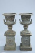 A HANDSOME PAIR OF CAST IRON URNS ON PLINTHS, of campana form, the plinths with a laurel wreath to