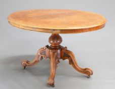 A VICTORIAN BURR WALNUT TILT-TOP LOO TABLE, the oval quarter-veneered moulded top raised on a carved