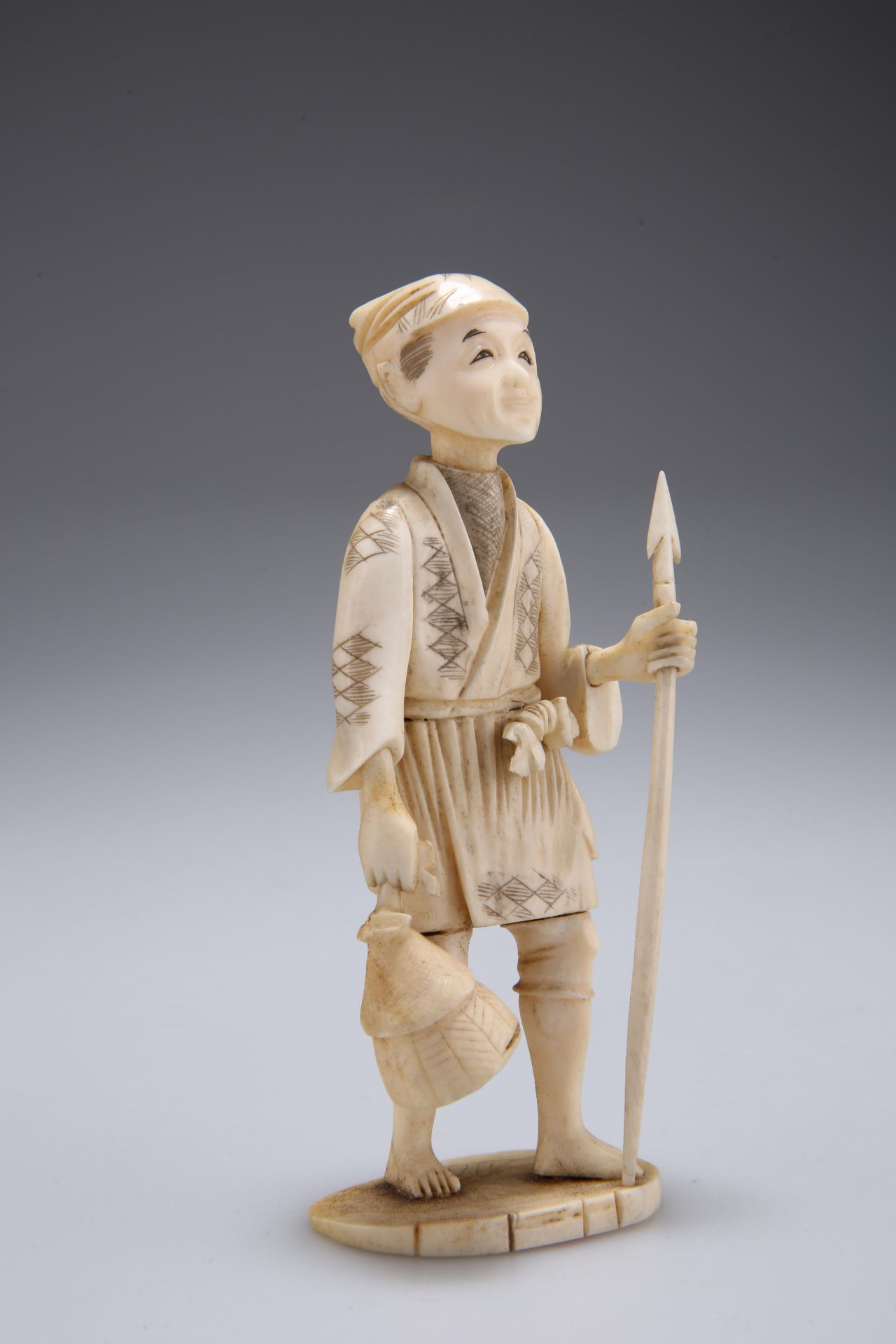 A JAPANESE IVORY OKIMONO, carved as a fisherman holding a spear and creel. 13cm high