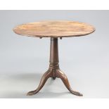 A GEORGE III OAK TILT-TOP TRIPOD TABLE, the circular top raised on a gun-barrel stem continuing to