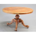 A VICTORIAN BURR WALNUT TILT-TOP LOO TABLE, the oval quarter-veneered moulded top raised on a carved