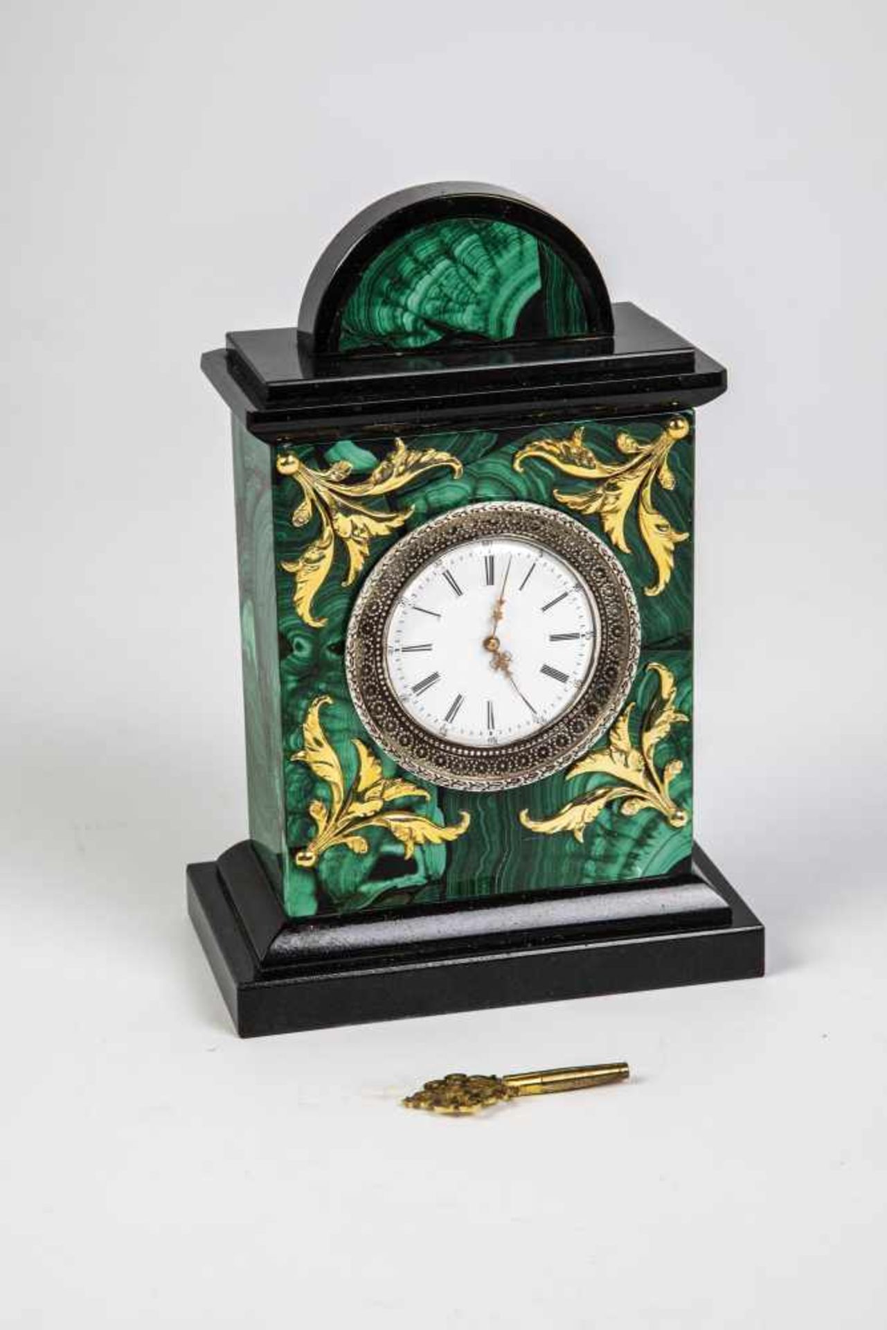 A malachite table clock. 20th century. Malachite and granite body with applied silver-giltfoliage.