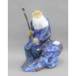 Chinese Shiwan glazed figure of a man sat upon a rock with a wooden staff in his hand, 24cm high