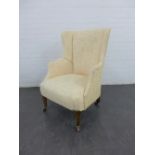 An upholstered wing back armchair with buttonback, on tapering mahogany legs with brass caps and