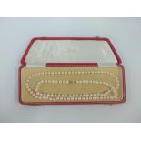 Long strand of cultured pearls with a 14 carat gold clasp fitting, in red leather box