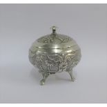 Eastern white metal circular box and cover, chased with tree and village pattern, on four out