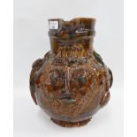 Brown glazed pottery jug with moulded heart shape face and religious motifs throughout, apparently