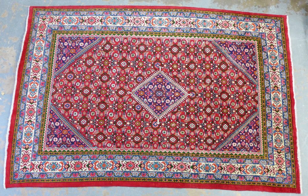 A large Eastern rug with red field and foliate pattern, flowerhead borders, 322 x 215cm