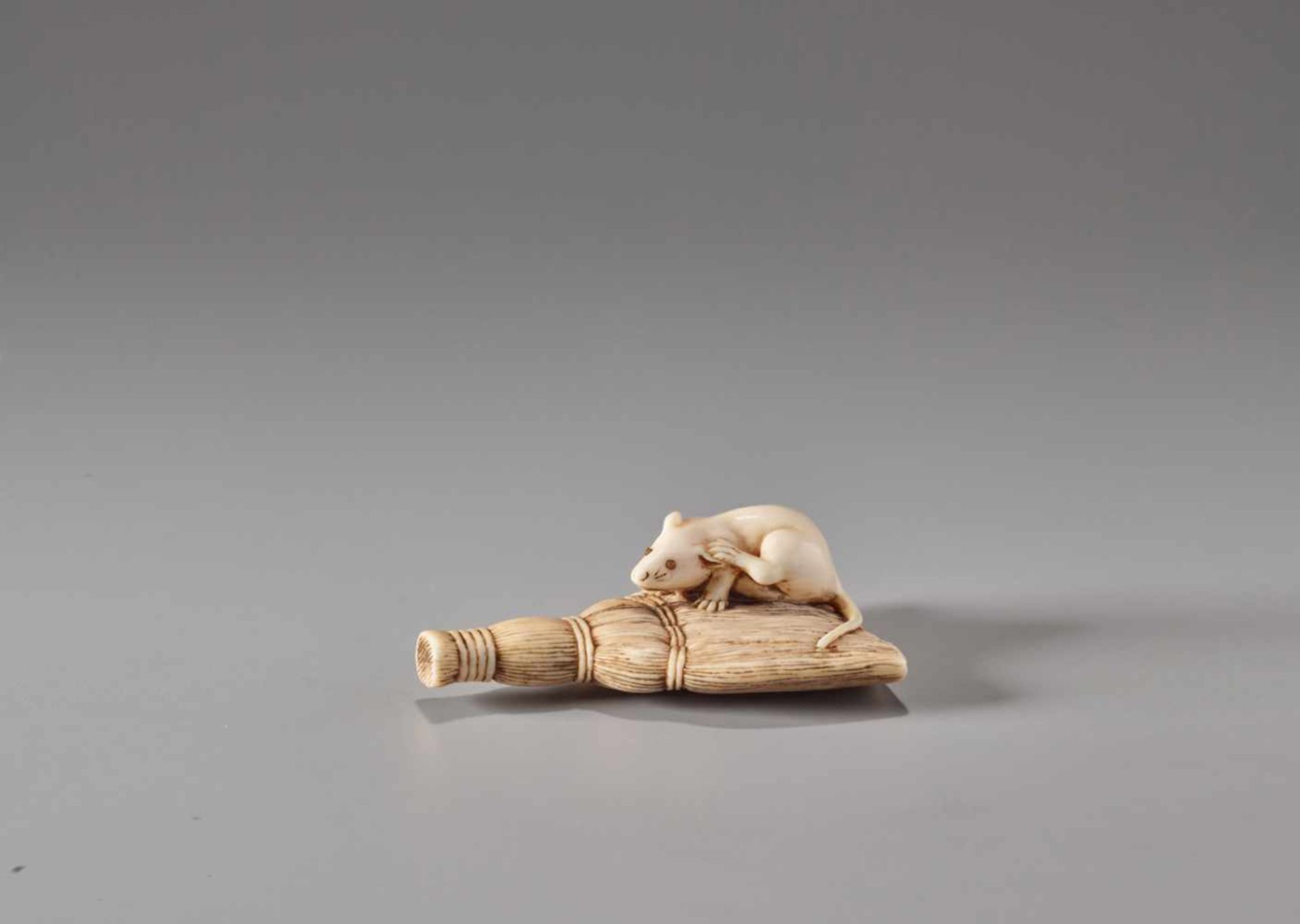 AN IVORY NETSUKE OF A RAT ON A BROOM