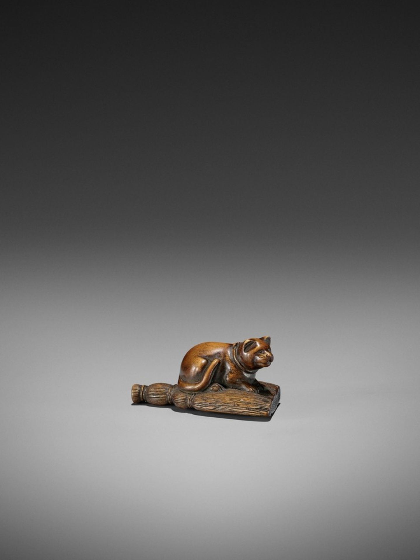 A WOOD NETSUKE OF A CAT ON A BROOM UnsignedJapan, early 19th century, Edo period (1615-1868)Finely