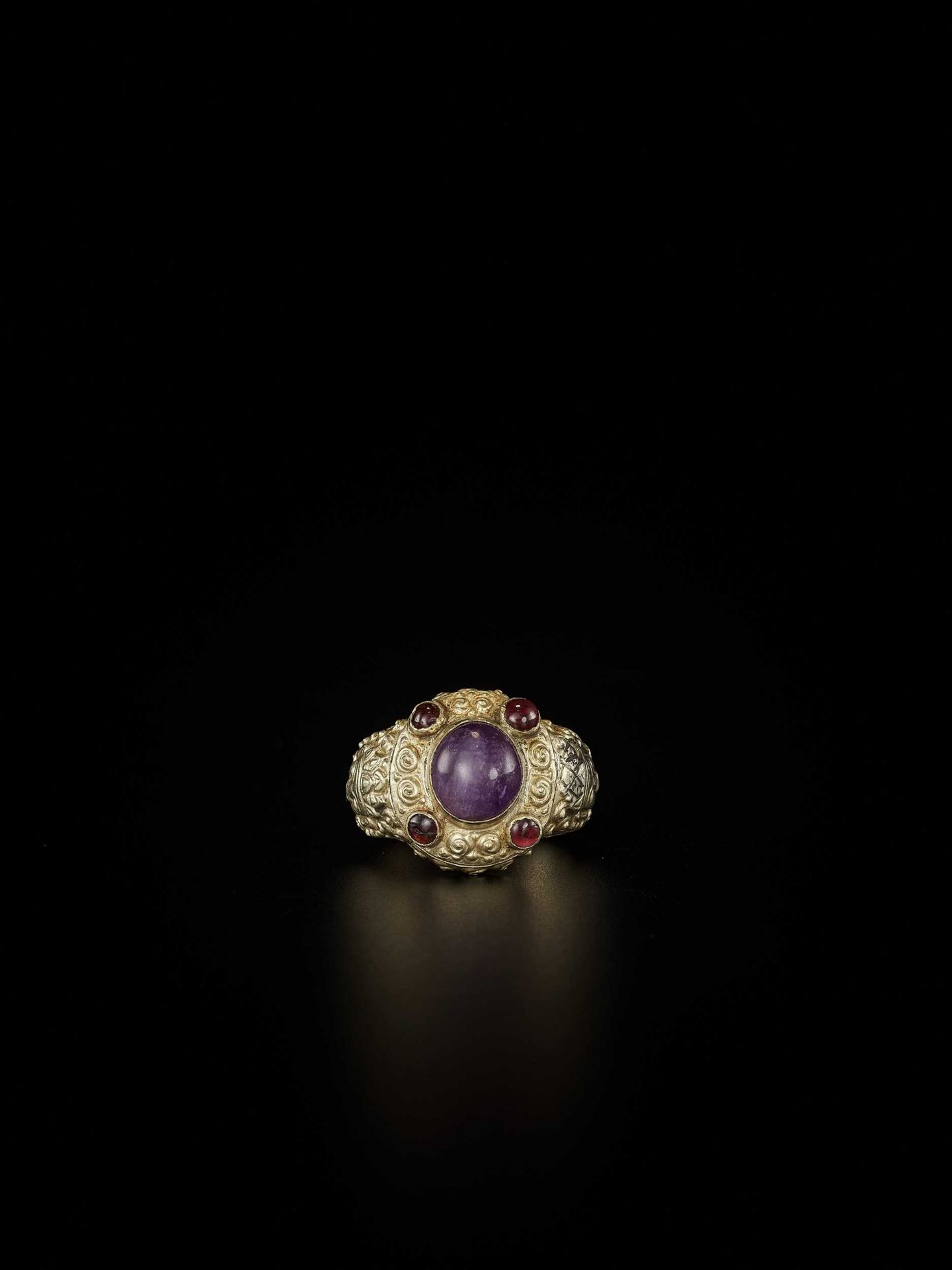 A CHAM AMETHYST AND GARNET-SET GOLD REPOUSSÉ RING WITH KING’S HEADS