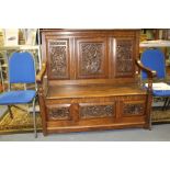 An early 20th century small oak settle, the three panelled back carved with dragon and heads, hinged