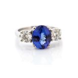 A tanzanite and diamond platinum three-stone ring, the central oval-cut tanzanite approx 2.78