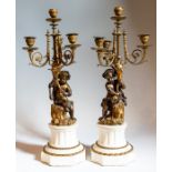 A pair of bronze and ormolu candelabra with white marble bases, each depicting children holding