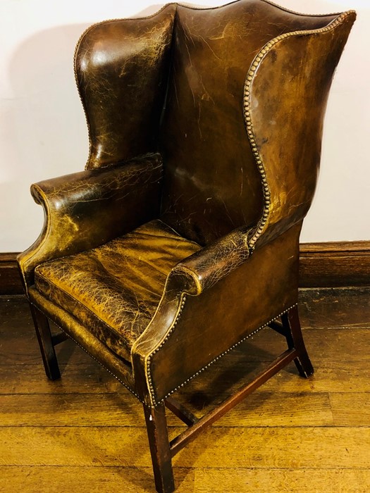 A George III brown leather wingback armchair, circa 1760, brass studs around the frame, scrolled