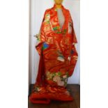 A red kimono (coat) with a vibrant design. Worn by a bride. Embellished in gold and silver thread