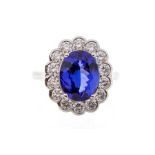 A tanzanite and diamond 18ct white gold cluster ring, the oval claw set tanzanite weighing a total