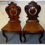 A pair of mid Victorian mahogany hall chairs, circa 1880, having cartouche backs, scroll carved