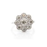 A diamond and platinum flower cluster ring, the collet set centre diamond surrounded by eight