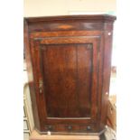 A George III oak wall hanging corner cupboard, the single panelled door enclosing two internal