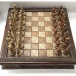 Chess set with moulded resin pieces with ornate board with drawers under.