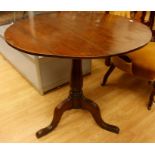 A George III oak tilt top tripod table, the plank top raised on a baluster turned column, standing