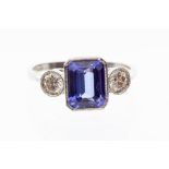 A tanzanite and diamond platinum ring, the rub over set emerald cut tanzanite weighing approx. 2.4
