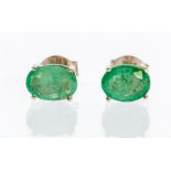 A pair of emerald and silver stud earrings, the oval emeralds measuring approx. 7.5mm x 5mm, set