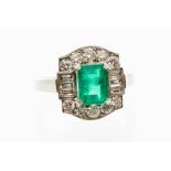 An emerald and diamond platinum dress ring, the central claw set emerald cut measuring approx. 8mm x