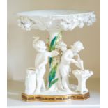 A Moore Brothers centrepiece, modelled as three putti forging arrows beneath a giant lily dish, 23.
