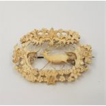A late 19th century carved ivory brooch, the centre pierced and finely carved as a stag in a forest,