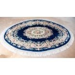 An oval rug, floral design in pink, cream and green on a deep blue ground, fringe border, 250cm by