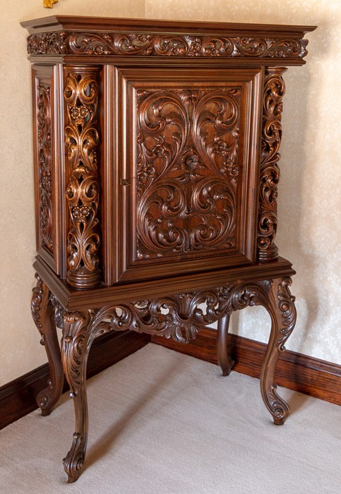 A mahogany drinks cabinet on stand, elaborately carved scrollwork throughout, retractable door