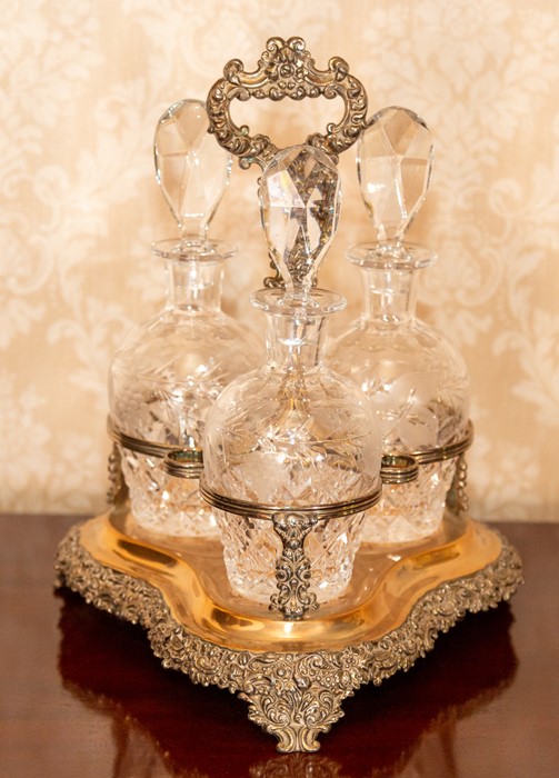 A triple glass decanter set in a plated foliate stand Note: located at the vendor's property in