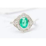An emerald and diamond platinum ring, the rub over set central oval cut emerald approx. 1carat,