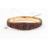 A Victorian Bohemian bangle, width approx 14mm, with garnets set throughout, gilt metal, hinged,