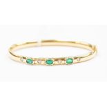 An 18ct gold hinged bangle with three oval collect set emeralds, with alternative flush set with