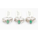 A collection of three emerald and diamond silver dress rings all of the same design, comprising oval