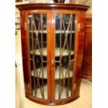 A George III mahogany and boxwood inlaid bow fronted glazed corner wall hanging cabinet, fitted with