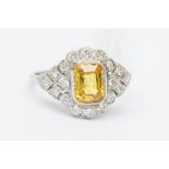 A yellow sapphire and diamond platinum ring, the rub over set central emerald cut sapphire approx.