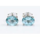 A pair of blue topaz and silver studs, comprising sky blue oval cut topaz approx. 7x 5mm, claw