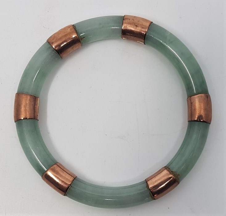 A jade slave bangle, c.1920's, with yellow metal mounts, external diameter 94mm.