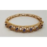 A 9ct. gold and sapphire set hinged bangle, of eliptical form with pierced tapering back and