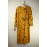 Hobeau. A long mustard coat, decorated with steam trains and adorned with padlock detail, 100% wool