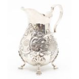 A late Victorian silver bombe milk jug, repousee scroll decoration, four hoof feet, gilt interior,