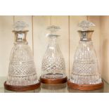A pair of silver collared cut glass decanters along with small decanter all on wooden casters
