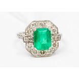 An Art Deco style emerald and diamond 18ct white gold dress ring, the central claw set emerald cut