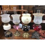 Four late 19th Century oil lamps with shades and funnels, ruby glass body example and ceramic