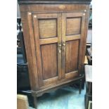 A George III oak and mahogany cross-banded corner cupboard, fitted with two doors enclosing fitted